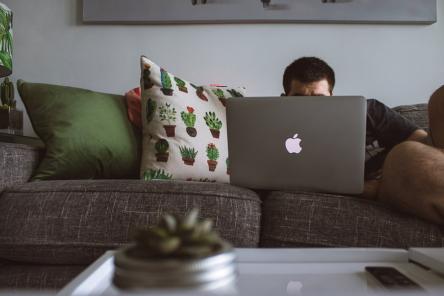 Man working on laptop on couch with cactus pillow