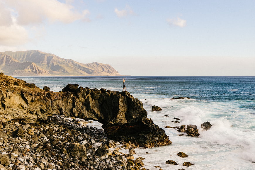 Person standing on rocky cliff overlooking ocean and mountains