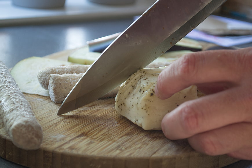 Close-up of hand slicing seasoned tofu on wooden cutting board