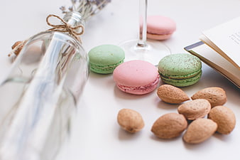 Pastel macarons and almonds on white table with book