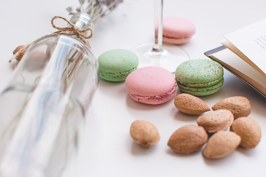Pastel macarons and almonds on white table with book