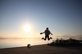 Silhouette of woman jumping joyfully at sunrise by the sea