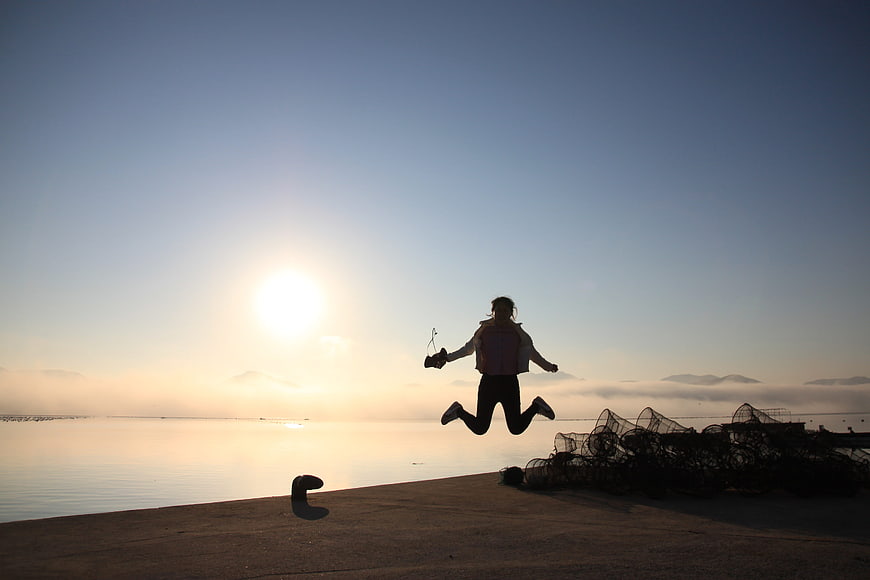 Silhouette of woman jumping joyfully at sunrise by the sea