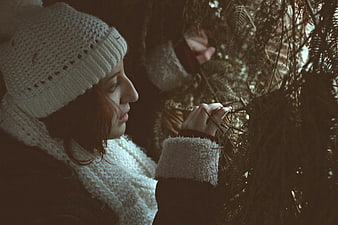 Woman in white knit hat touching pine branches in forest
