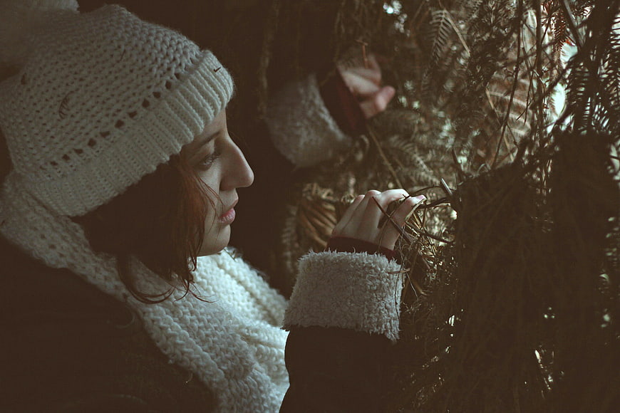 Woman in white knit hat touching pine branches in forest