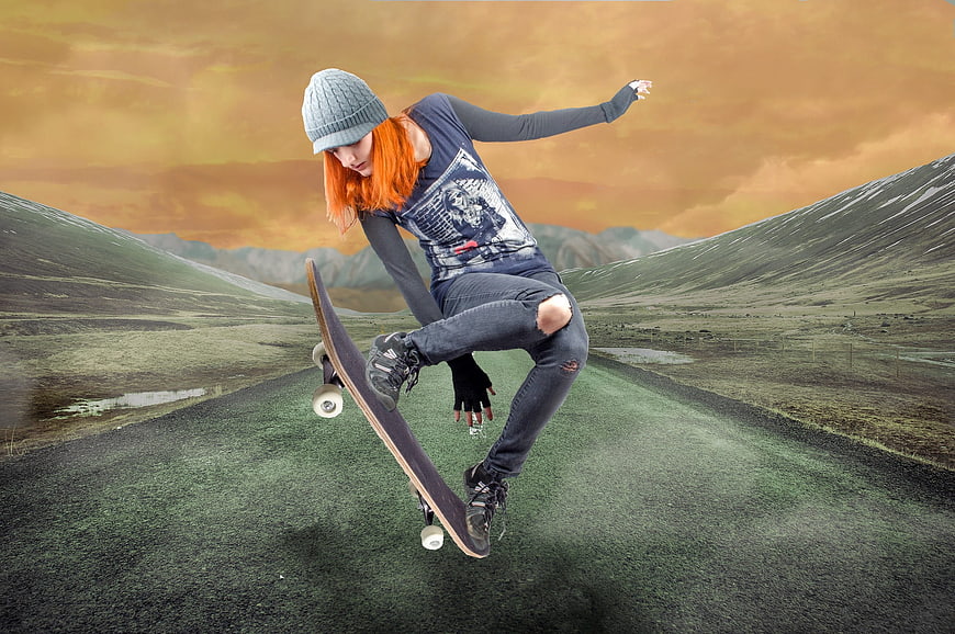 Young woman performing skateboard trick on rural road at sunset