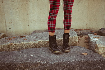 Woman's legs in red plaid pants and black boots on rocks