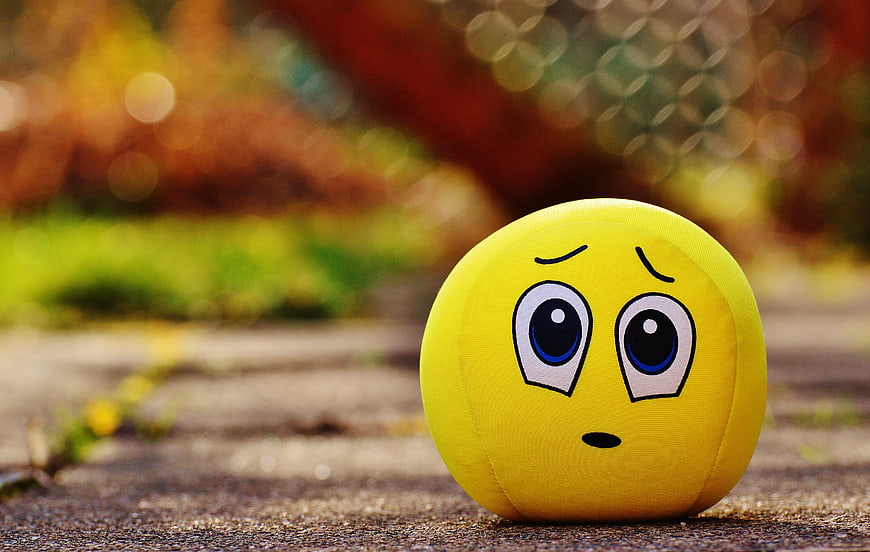 Yellow plush emoji ball with sad expression on pavement