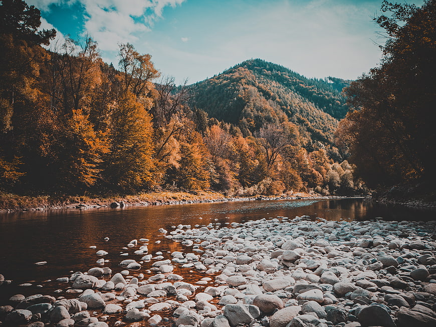 Serene Autumn River Landscape with Rocky Shore and Forested Mountains