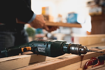 Green electric drill on wooden workbench with carpenter in background