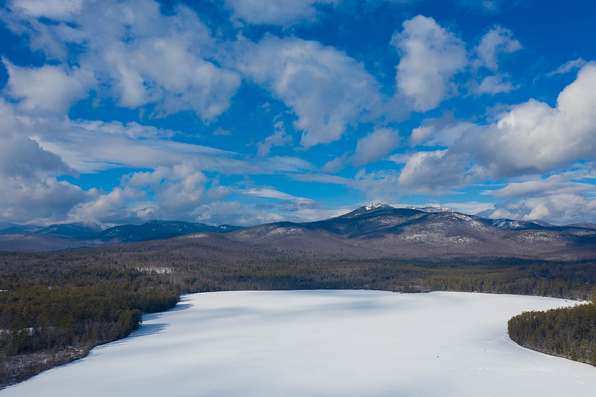 Aerial view of frozen lake surrounded by forest and mountains