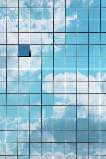 Modern glass building facade with open window reflecting blue sky