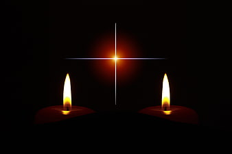 Two lit candles with glowing cross on black background
