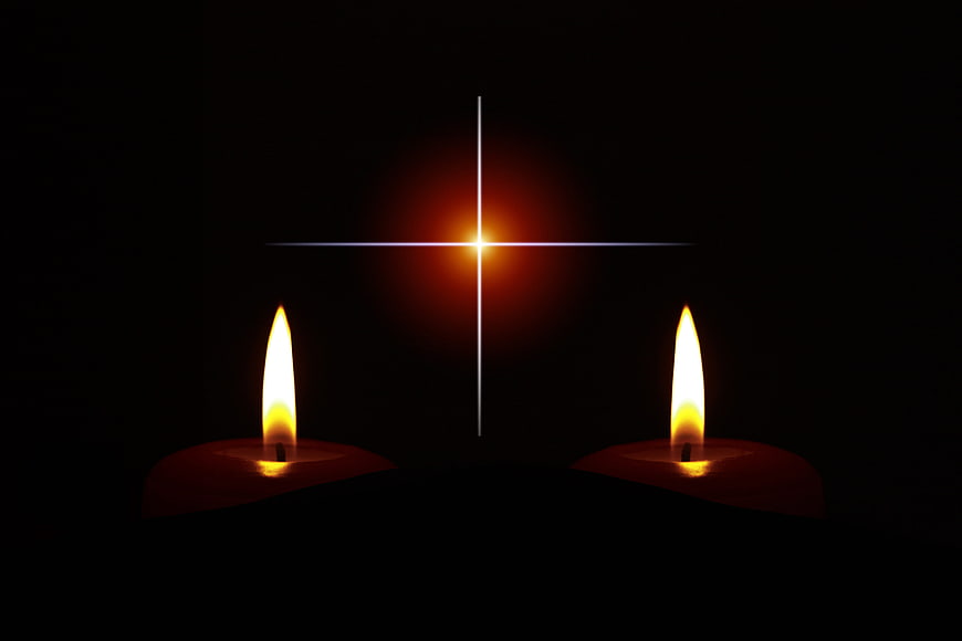 Two lit candles with glowing cross on black background