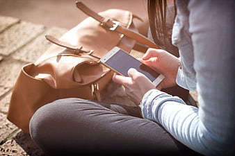 Woman using smartphone with leather backpack outdoors