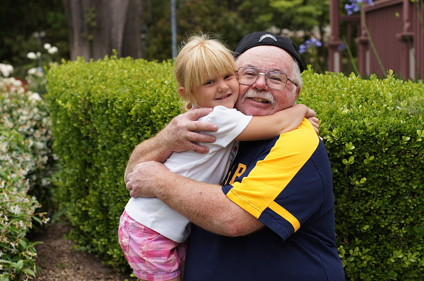 Senior Grandfather Hugging Young Blonde Granddaughter In Garden