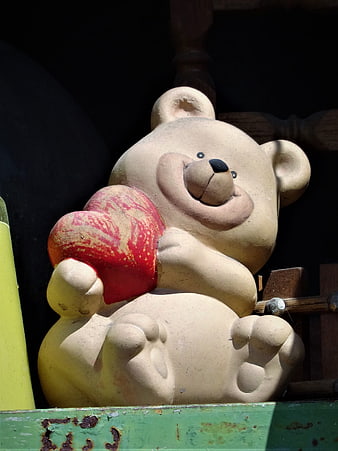 Vintage stone teddy bear sculpture holding a red heart