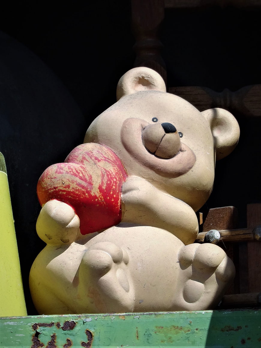 Vintage stone teddy bear sculpture holding a red heart