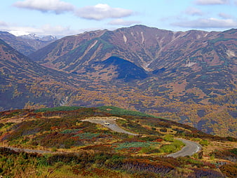 Winding mountain road through autumn landscape with distant peaks