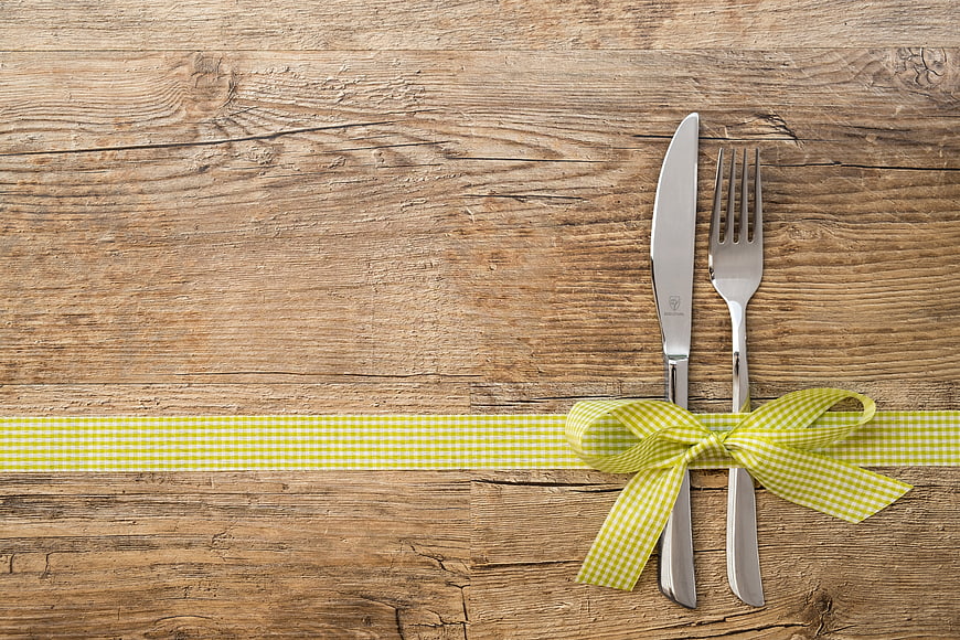Silver cutlery tied with yellow gingham ribbon on rustic wood