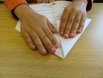 Child's Hands Folding Paper Airplane on Wooden Desk