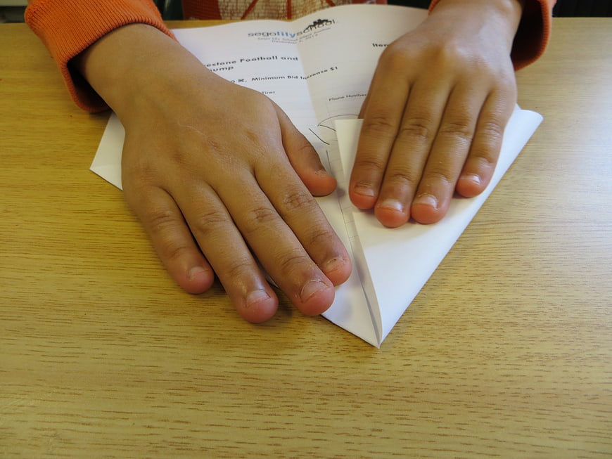Child's Hands Folding Paper Airplane on Wooden Desk