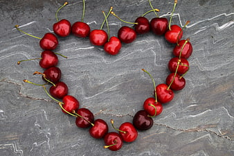 Fresh red cherries arranged in a heart shape on gray marble