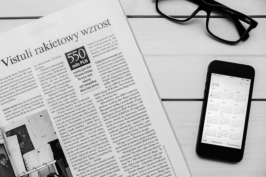 Black and white flat lay of newspaper, smartphone, and glasses