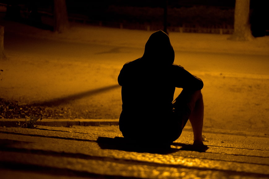 Silhouette of Lonely Hooded Man Sitting Alone at Night