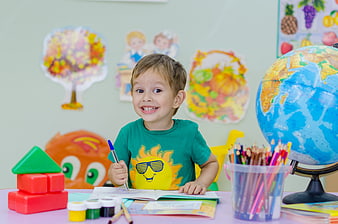 Happy young boy drawing at school desk with globe and toys
