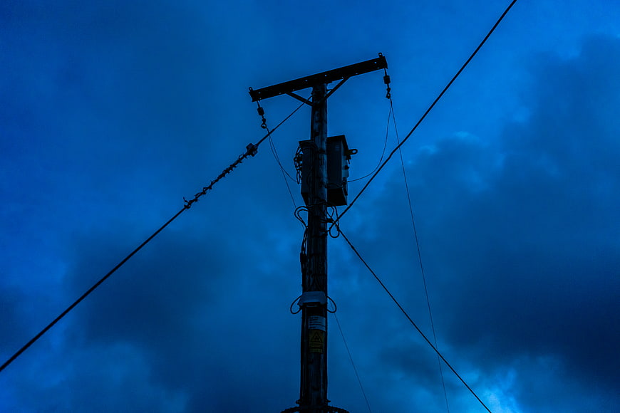 Silhouette of utility pole against dramatic blue sky