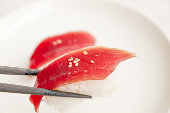Close-up of Tuna Sushi with Sesame Seeds Held by Wooden Chopsticks