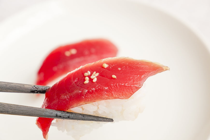 Close-up of Tuna Sushi with Sesame Seeds Held by Wooden Chopsticks