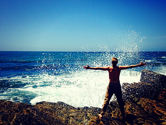 Man with Arms Outstretched on Rocky Ocean Shore