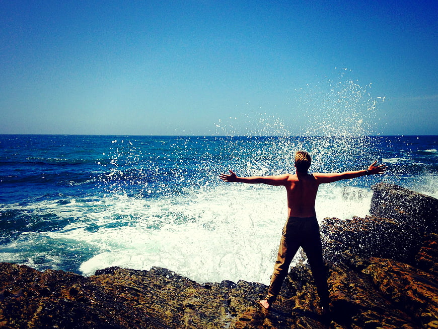 Man with Arms Outstretched on Rocky Ocean Shore