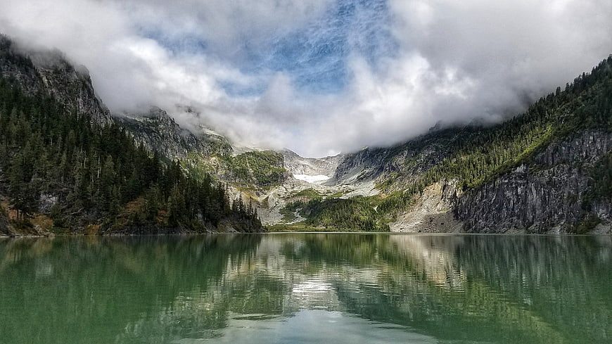Serene Alpine Lake with Mountain Reflections and Cloudy Sky