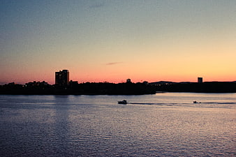 Silhouette of city skyline at sunset over water with boats