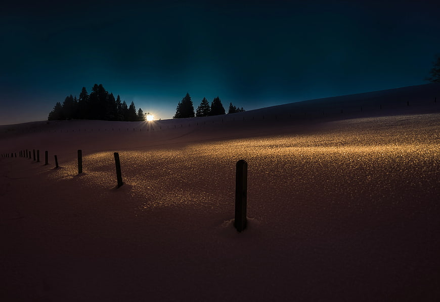 Snowy Winter Landscape with Wooden Fence Posts at Dusk