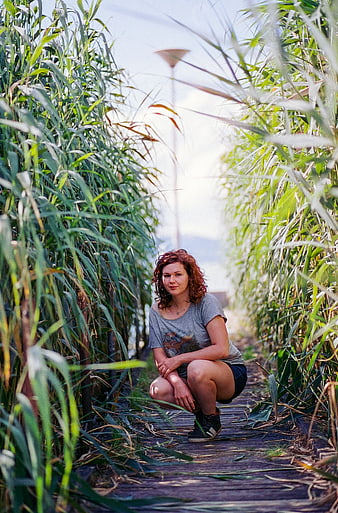 Redhead Woman Squatting in Tall Green Reeds