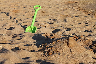 Green plastic shovel stuck in sand on a sunny beach