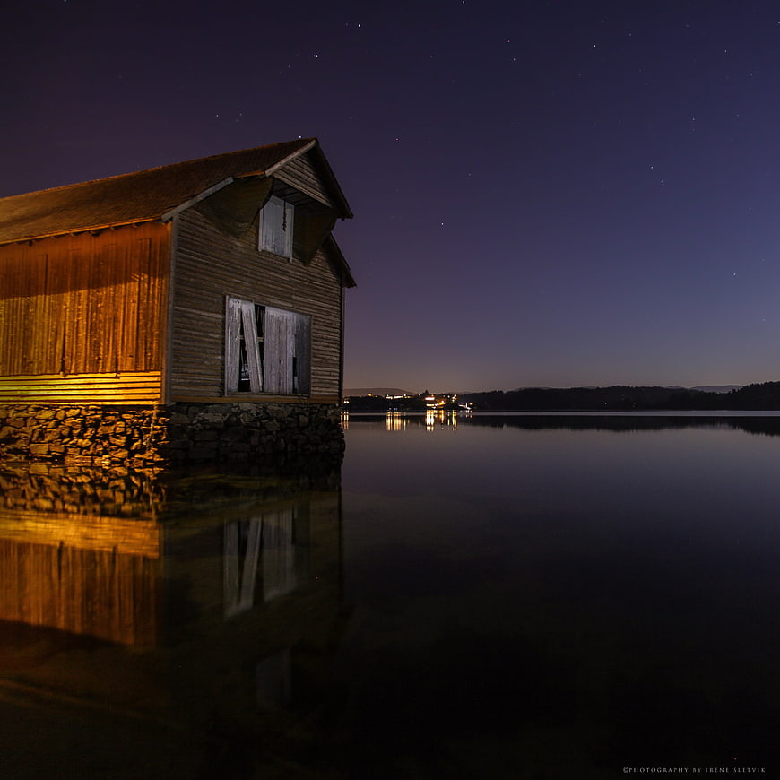 Illuminated wooden boathouse at night with starry sky