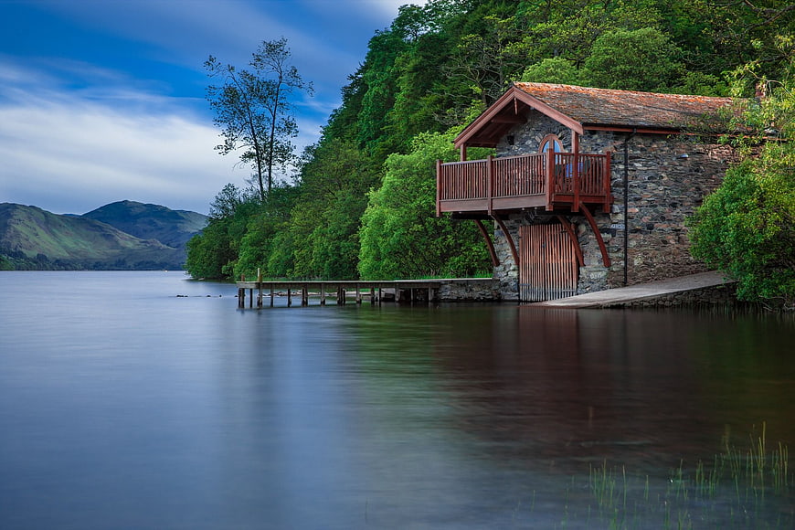 Stone boathouse on calm lake with wooden pier and forest