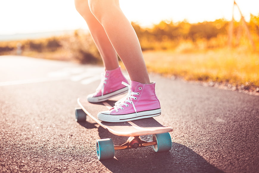 Close-up of pink sneakers on a longboard on a sunny road