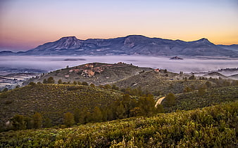 Misty mountain landscape at sunrise with rolling hills and fog