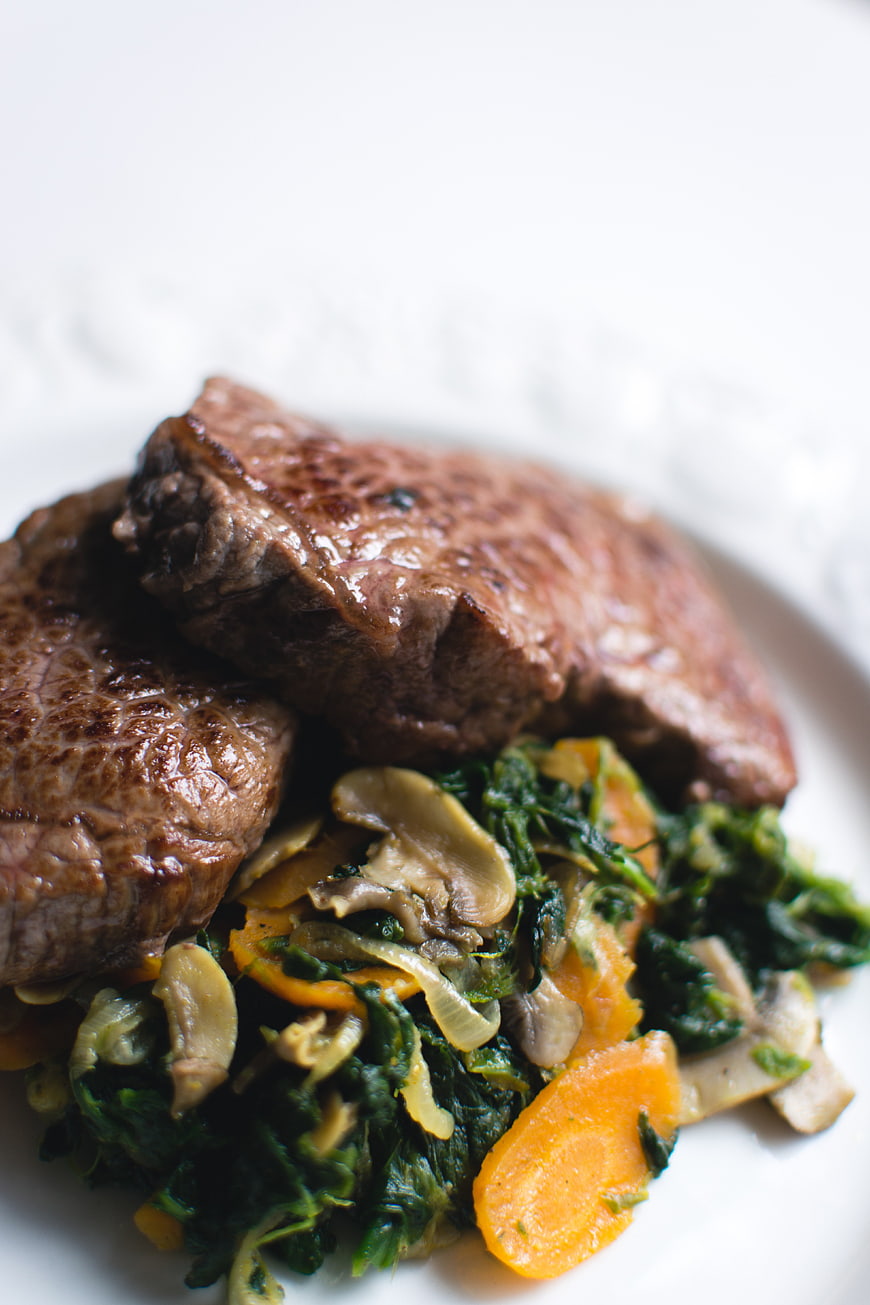 Close-up of grilled steak with sauteed vegetables on white plate