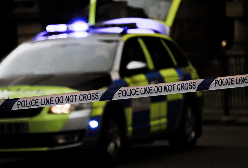 Police car with flashing lights behind crime scene tape at night