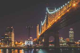 Night view of Manhattan Bridge with city skyline and water reflections