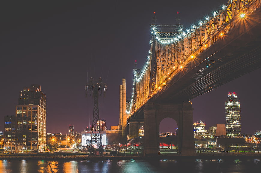 Night view of Manhattan Bridge with city skyline and water reflections