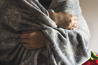 Close-up of hands clutching a gray patterned blanket