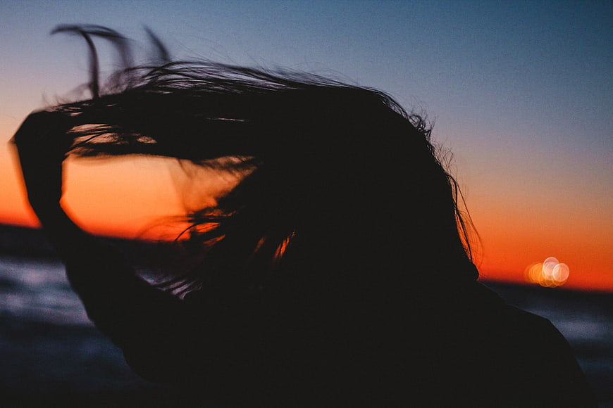 Silhouette of woman with windblown hair against sunset ocean
